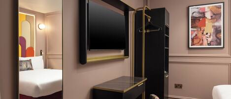 A hotel room with a bed, a desk, a mirror, a TV, and a painting on the wall.
