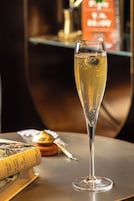 Ein Glas Champagner auf einem Tisch, im Hintergrund liegen ein Buch und eine Speisekarte.