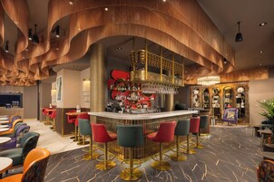 A bar area with a curved counter, red and green bar stools, and a variety of bottles and glasses on shelves.