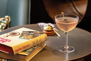 Ein Buch mit dem Titel „Agatha Christie“ und ein Cocktailglas auf einer Tischplatte.
