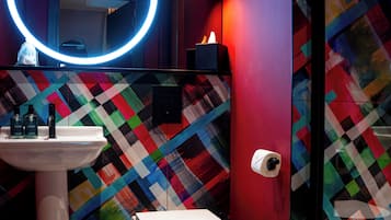 Une salle de bain avec un lavabo blanc, des toilettes et un mur orné d’un motif géométrique coloré.