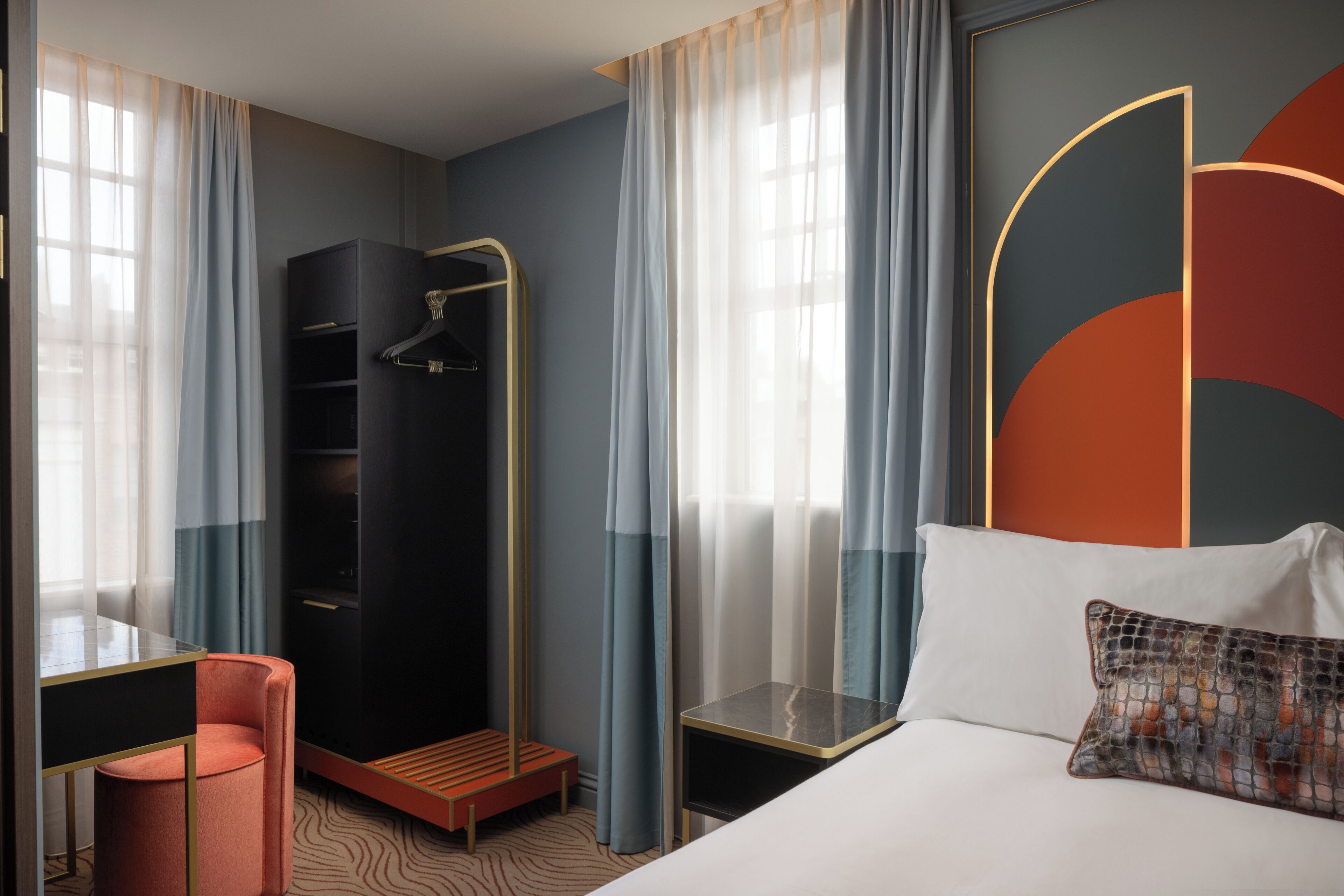 A modern hotel room with a bed, a seating area with a chair, a wardrobe, and a shower area.