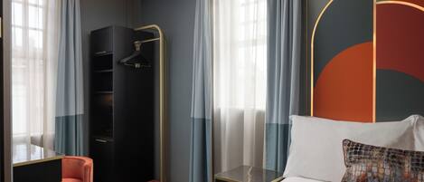 A modern hotel room with a bed, a seating area with a chair, a wardrobe, and a shower area.