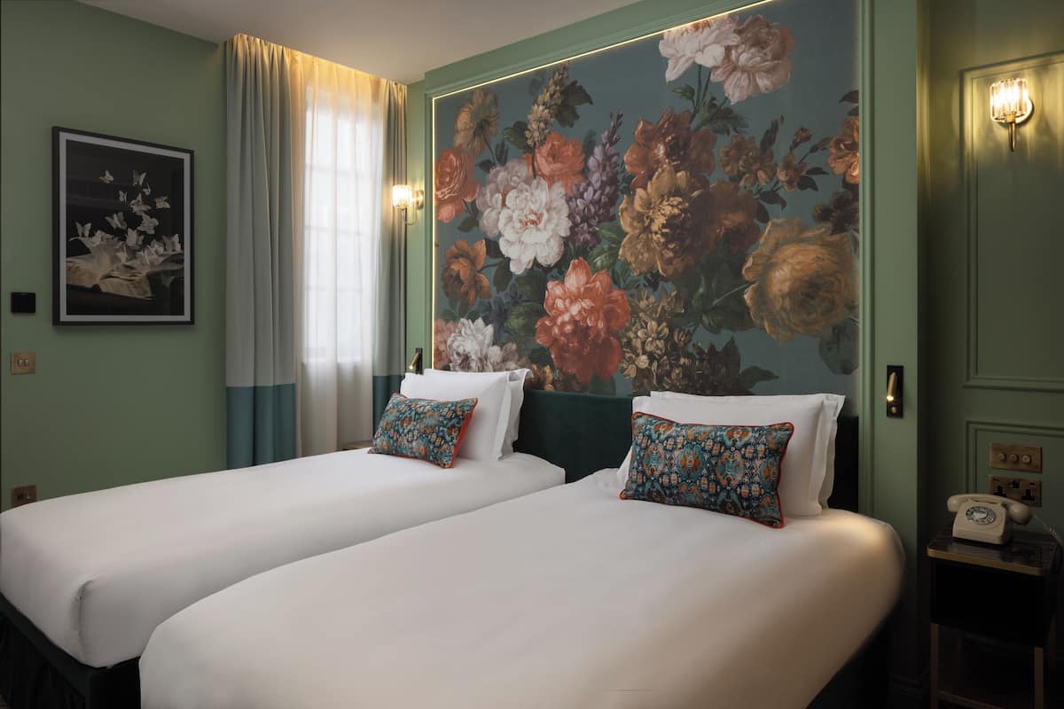 Een hotelkamer met twee bedden, bloemenbehang, een schilderij en een telefoon op een nachtkastje.