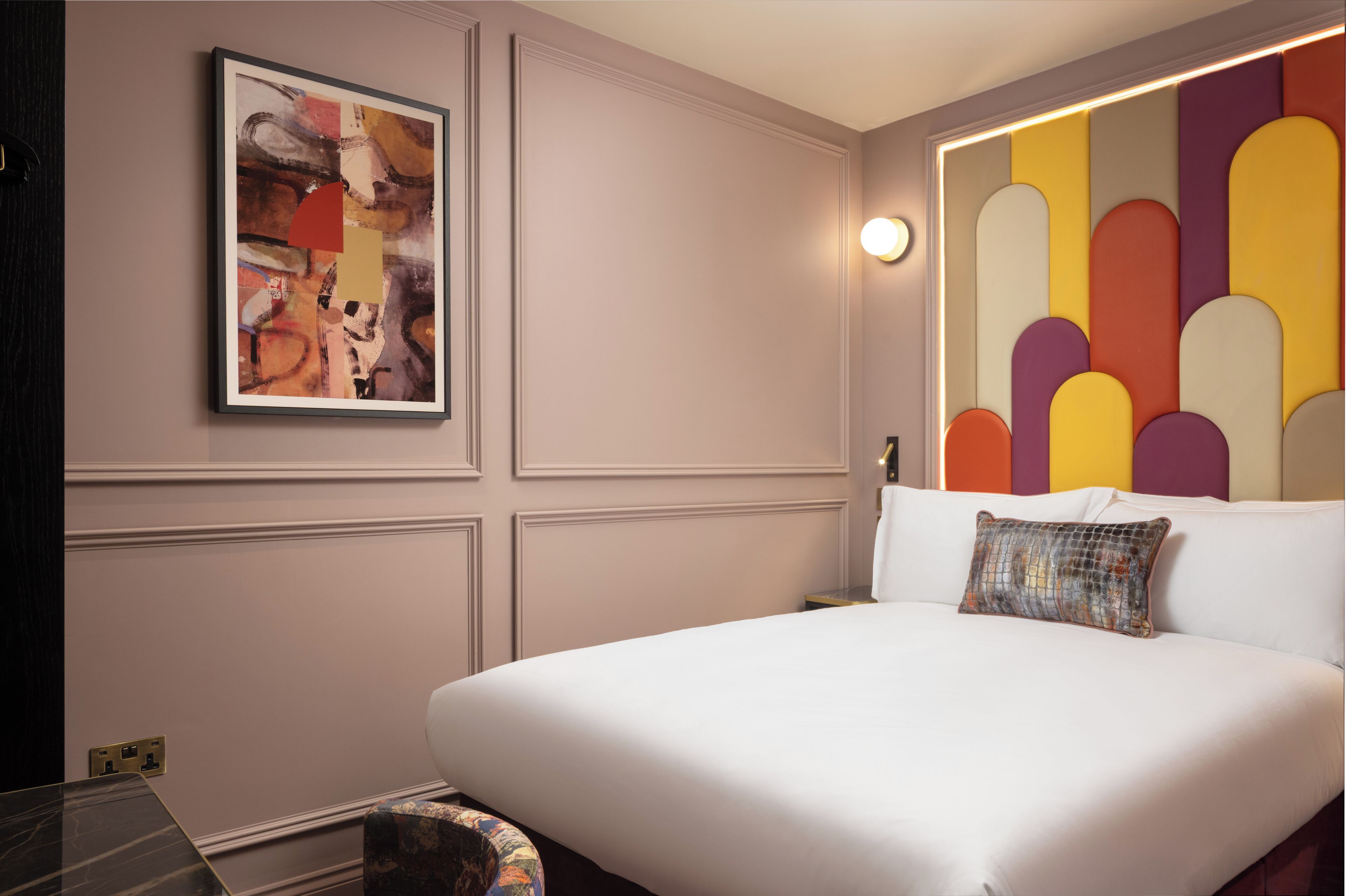 Et moderne hotelværelse med en stor seng, et indrammet abstrakt maleri og et unikt geometrisk vægpanel.