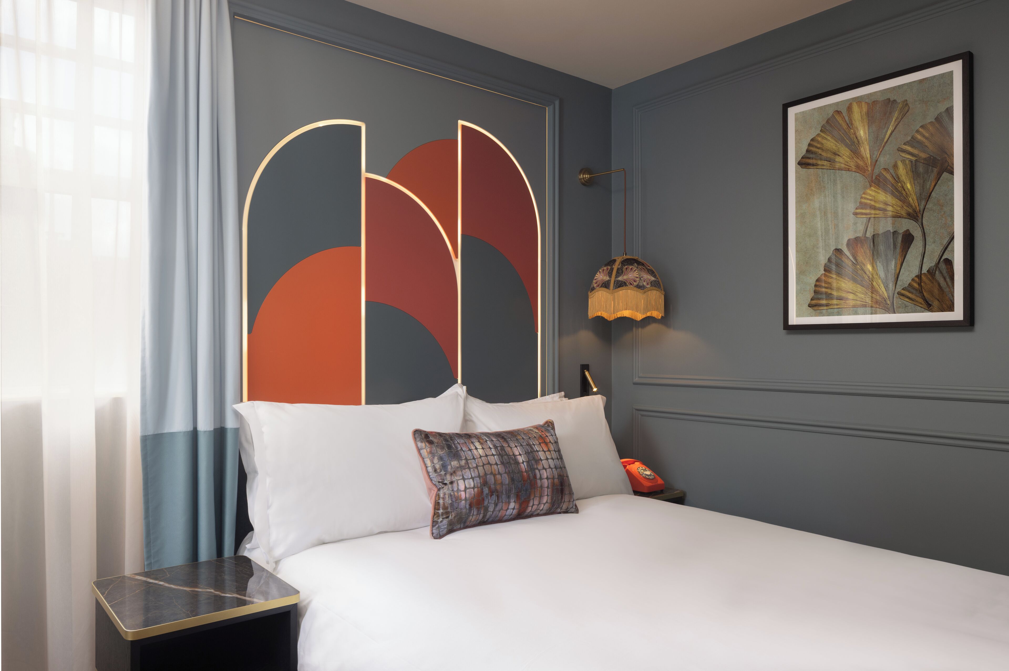 Een hotelkamer met een bed, nachtkastje, lamp en een schilderij aan de muur.
