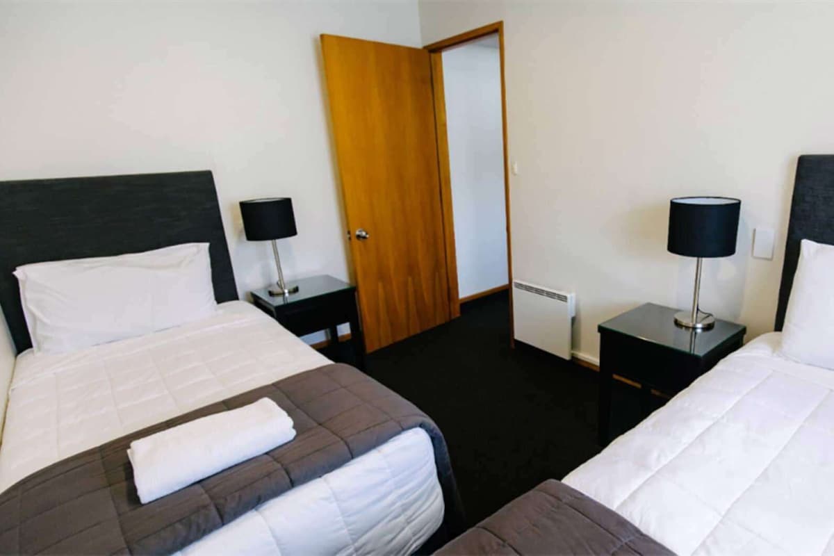 Een hotelkamer met twee bedden, een houten deur, een radiator en twee nachtkastjes met lampen.