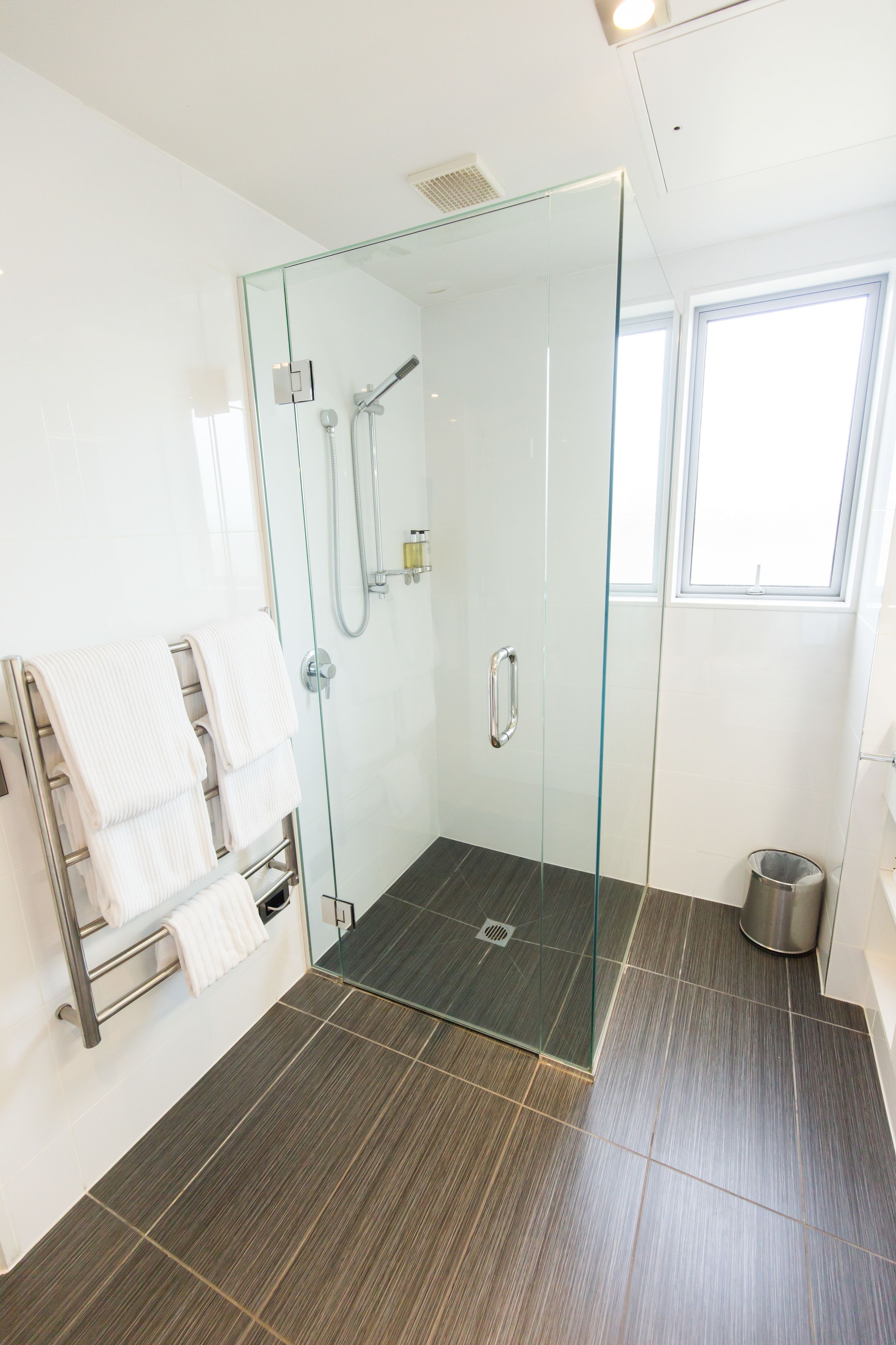 Un baño moderno con cabina de ducha de vidrio, un perchero con toallas blancas y una ventana que proporciona luz natural.