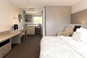 Habitación de hotel con cama, escritorio, silla, armario y kitchenette.