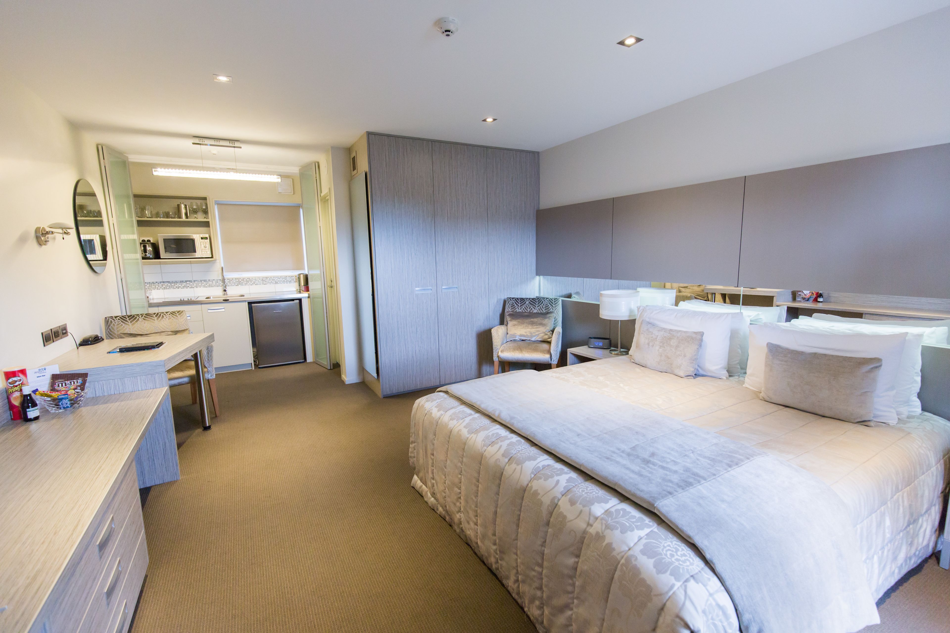 A hotel room with a large bed, a desk with a chair, a microwave, and a minibar.