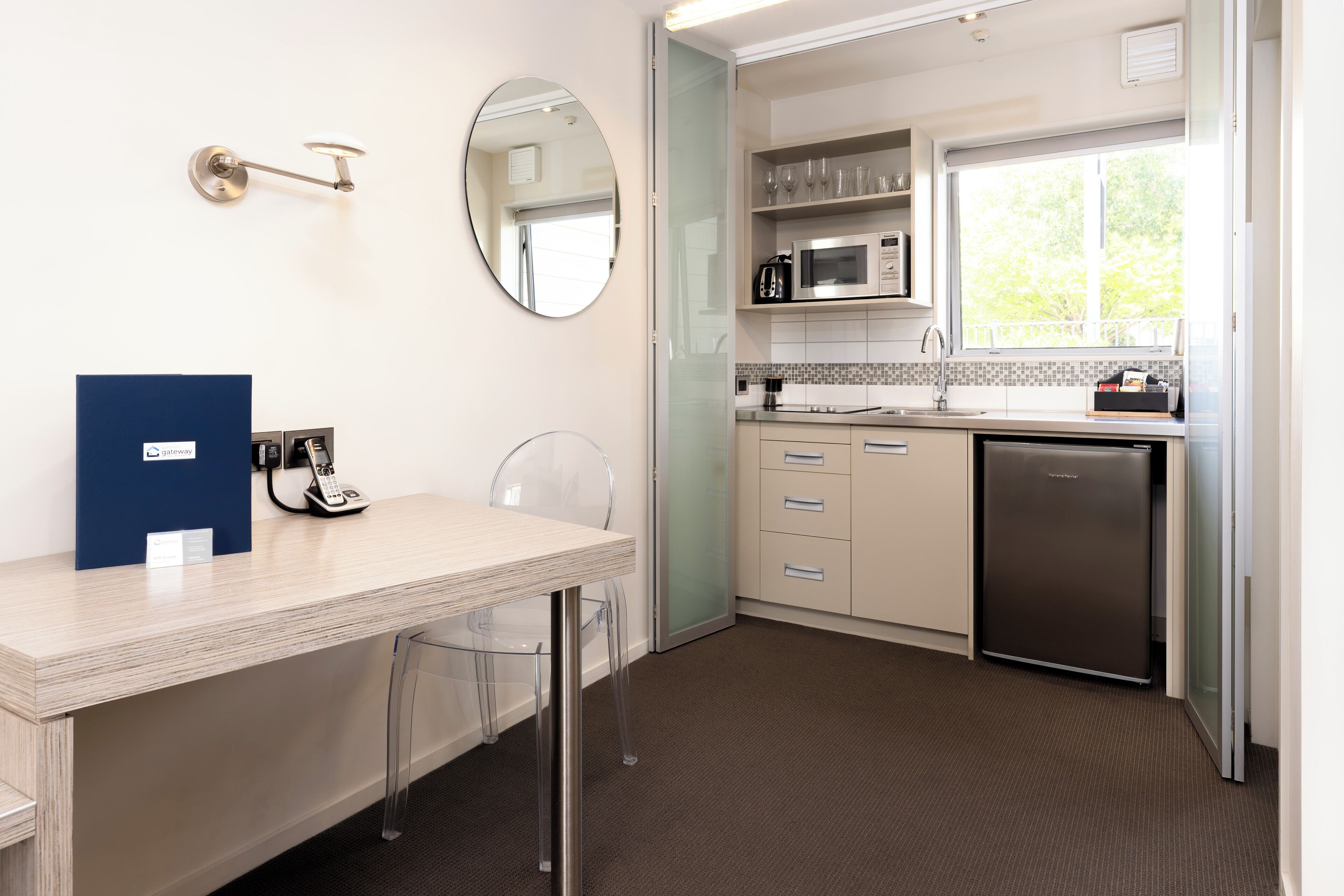 A modern kitchen with a microwave, coffee maker, and refrigerator. There is a glass door leading to the dining area.
