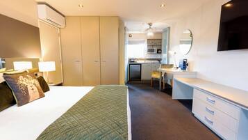 Een hotelkamer met een bed, bedlampjes, een bureau, een stoel, een kitchenette en een aan de muur bevestigde televisie.