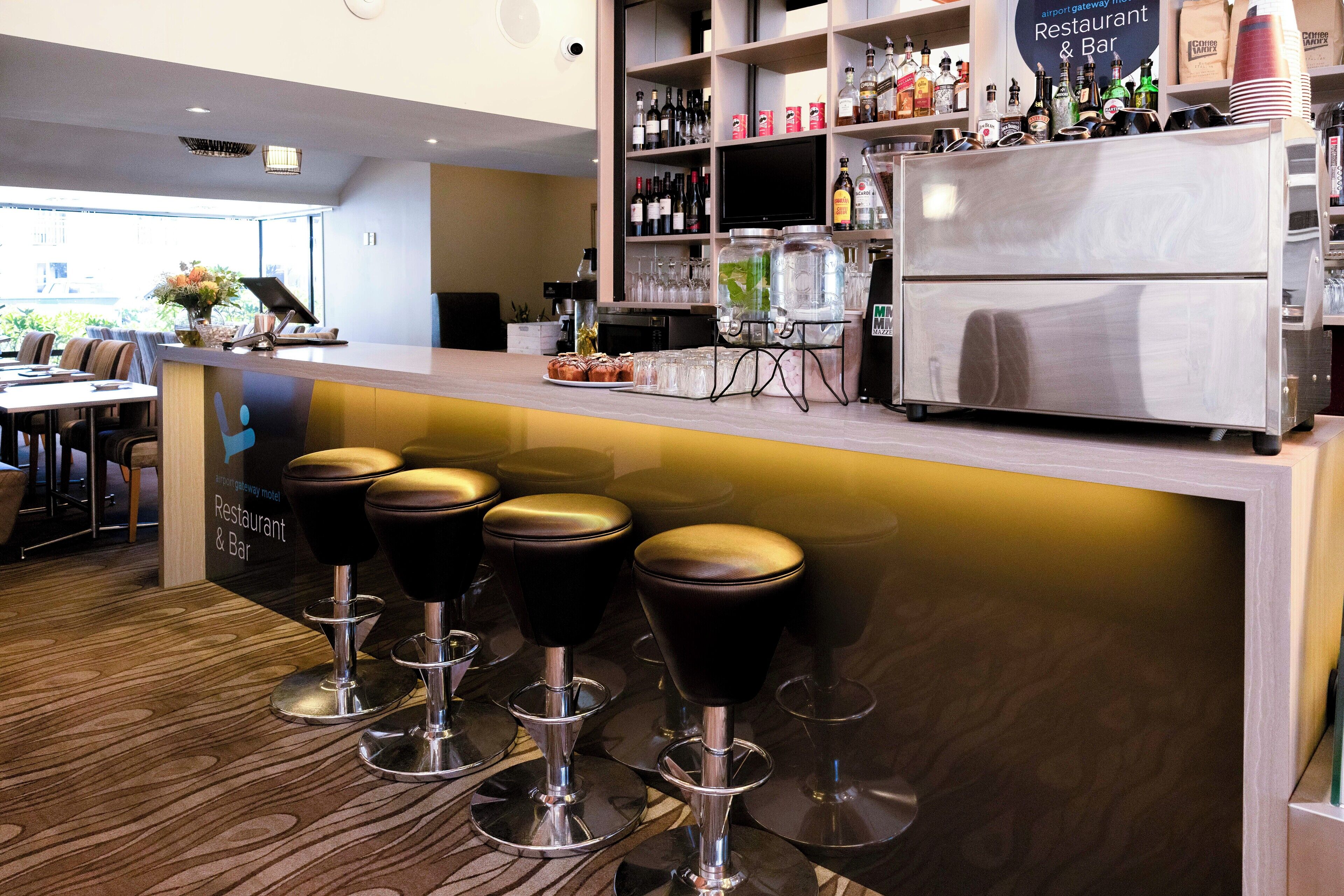 Un área de bar con taburetes, un refrigerador y estantes llenos de botellas y vasos.