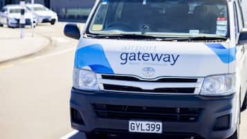 A white and blue van with "airport gateway" and "Motel - Christchurch" on the side, parked on a street.