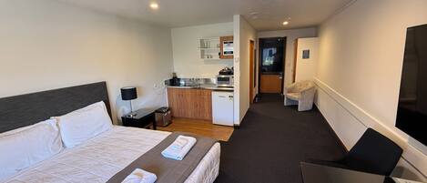 Habitación de hotel con cama, escritorio, silla, televisión, kitchenette y baño.