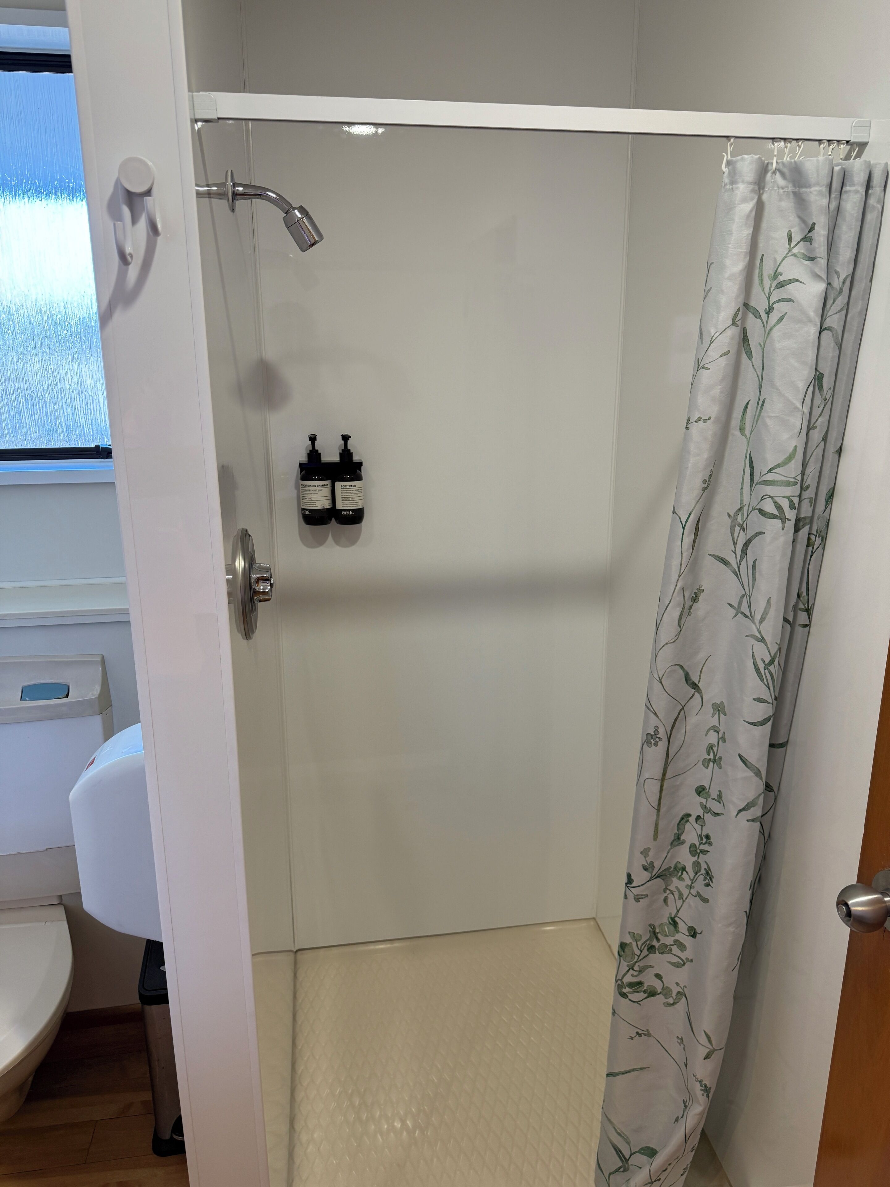A shower area with a glass door, a white sink, and a window with a view.