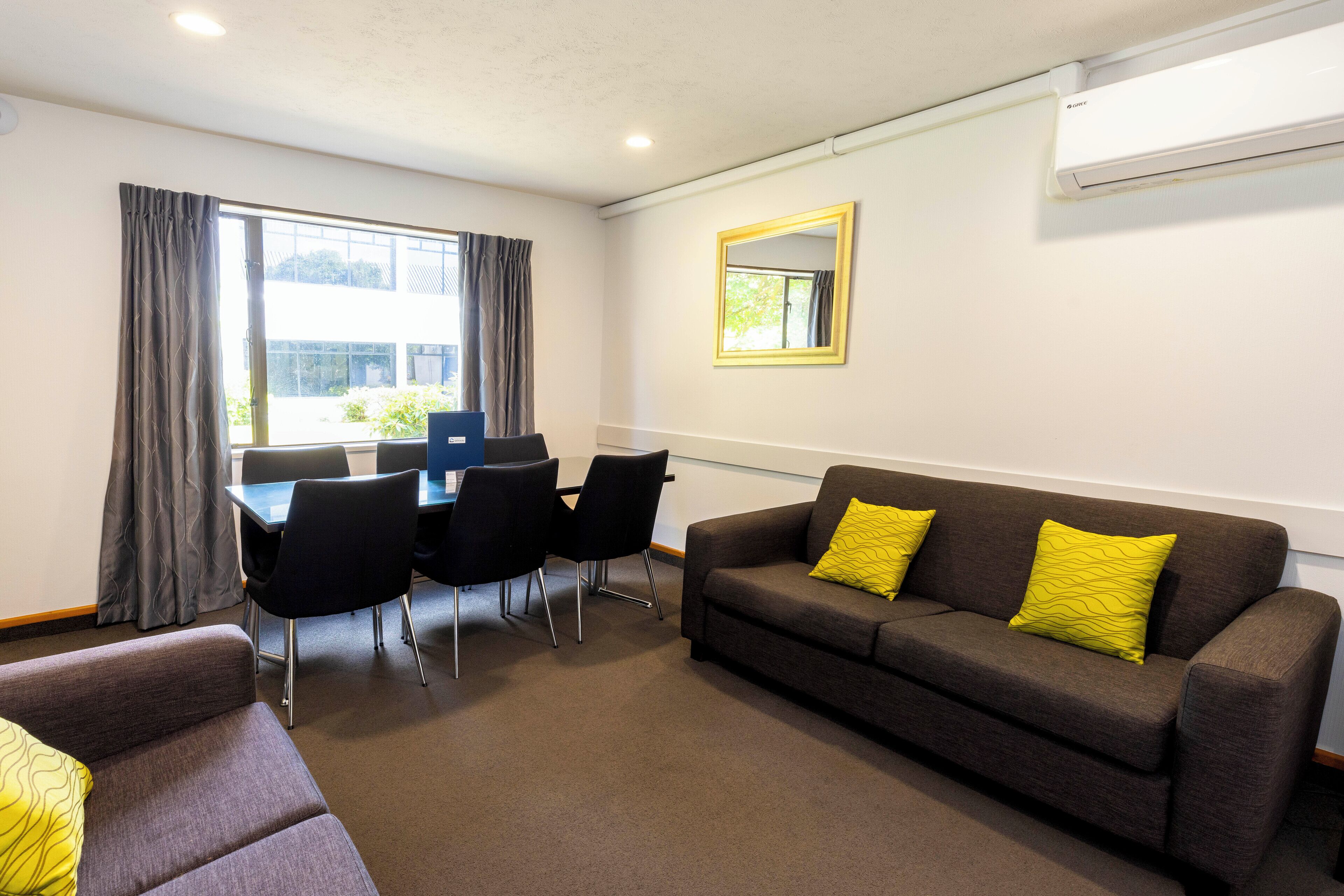 A furnished room with a sofa, a dining table with chairs, and a large window with curtains.