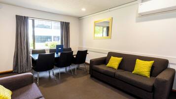 A furnished room with a sofa, a dining table with chairs, and a large window with curtains.
