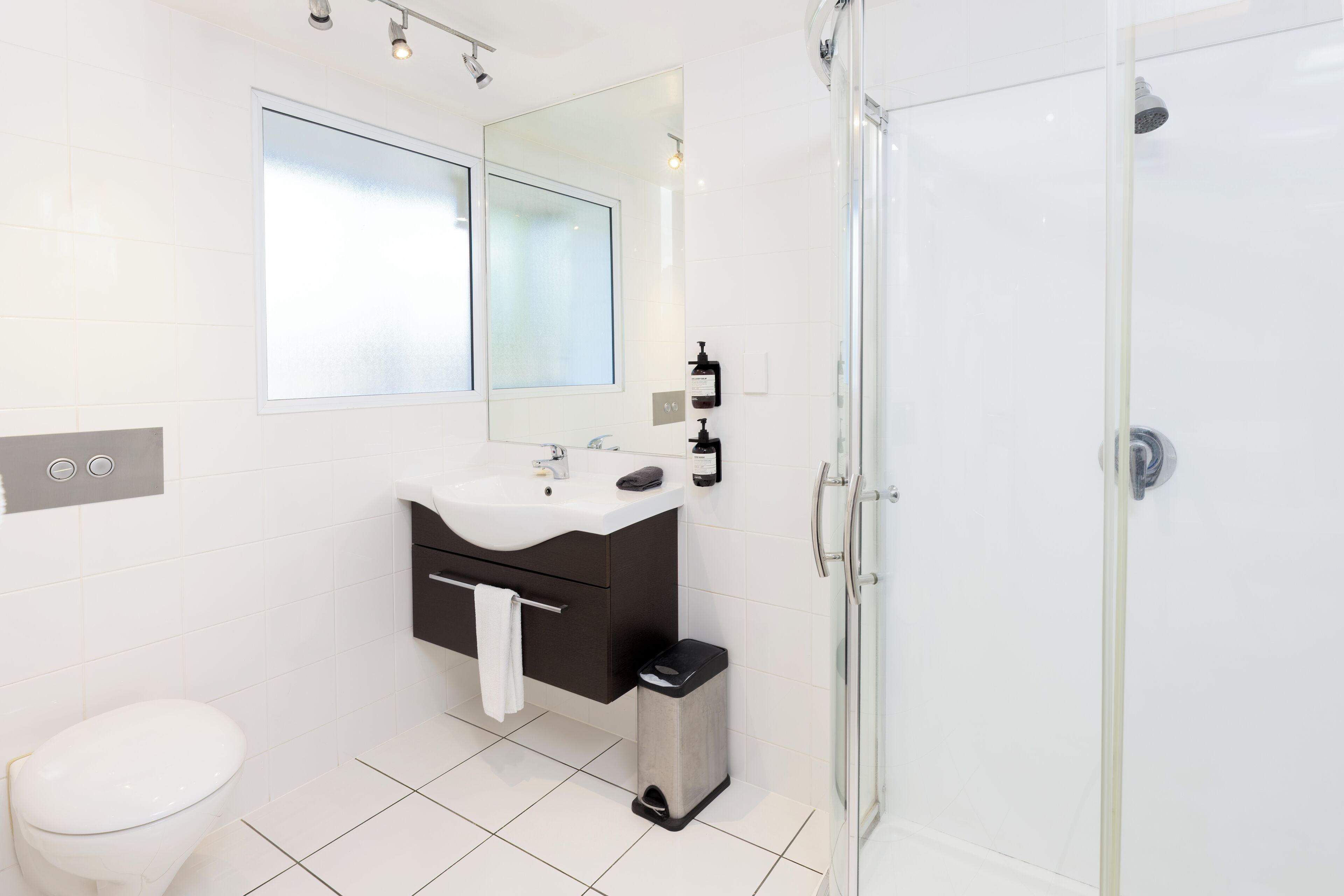 A modern bathroom with a white sink, dark vanity, mirror, and a glass shower enclosure.