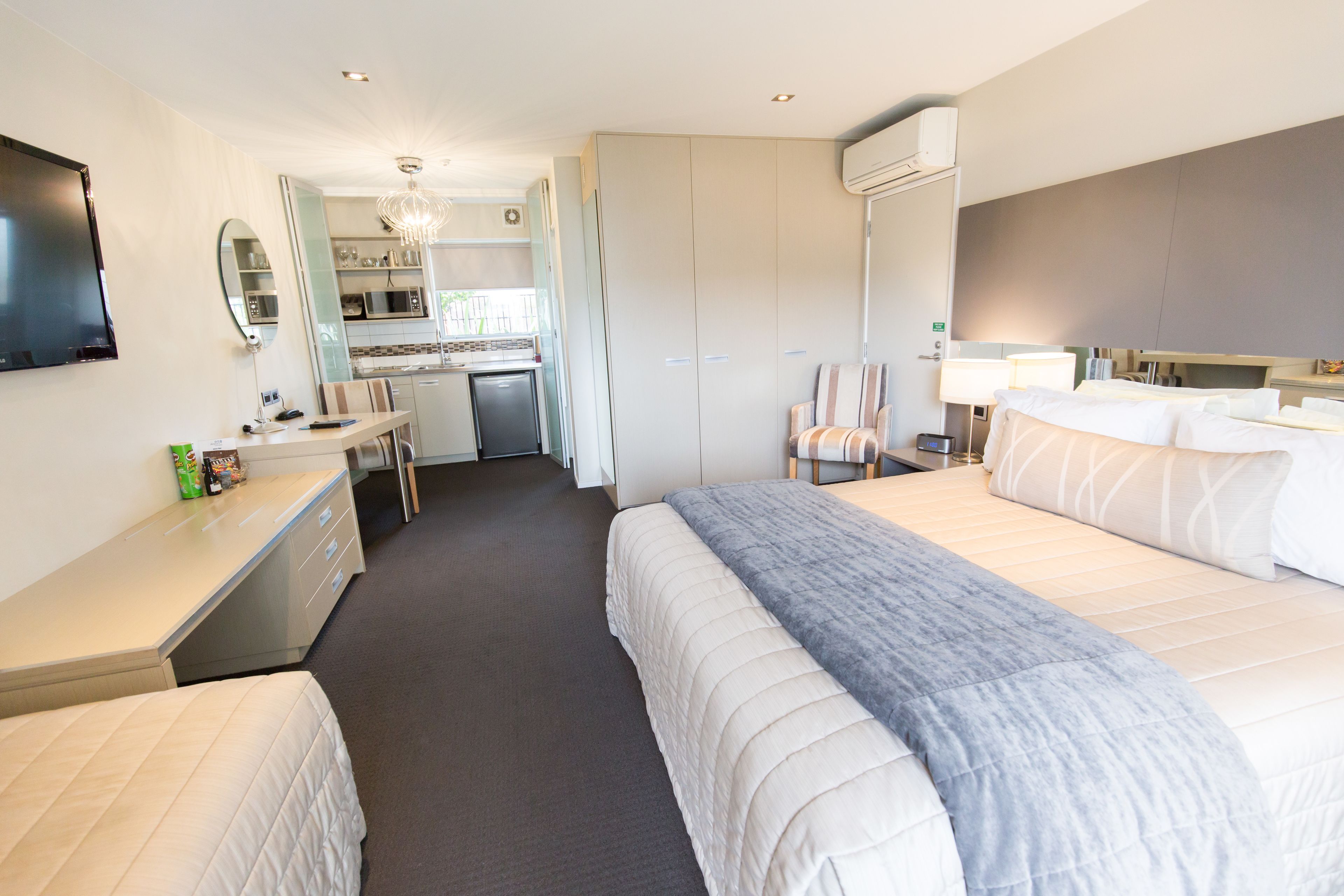 A hotel room with a bed, bedside table, and a small kitchenette.
