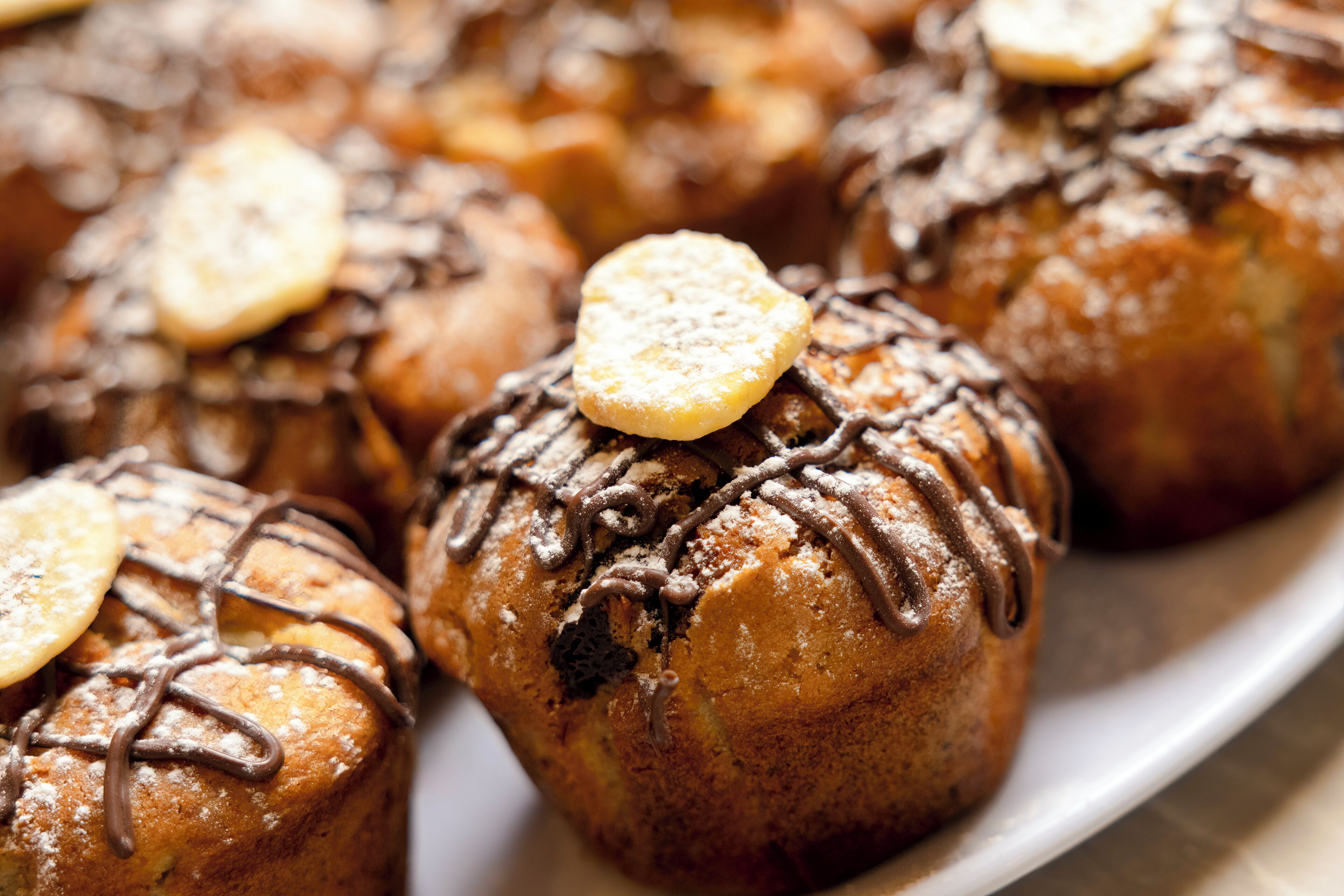 A plate of muffins with chocolate drizzle and a biscuit on top.
