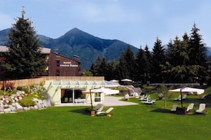 A hotel with a mountain backdrop, outdoor seating, and a well-maintained garden. - Centro Pineta Family Hotel & Wellness (Pinzolo)