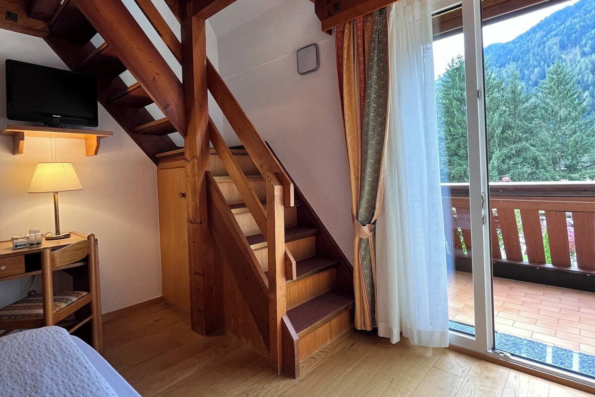 A wooden interior with a staircase, a bed, a TV, and a balcony with a mountain view.
