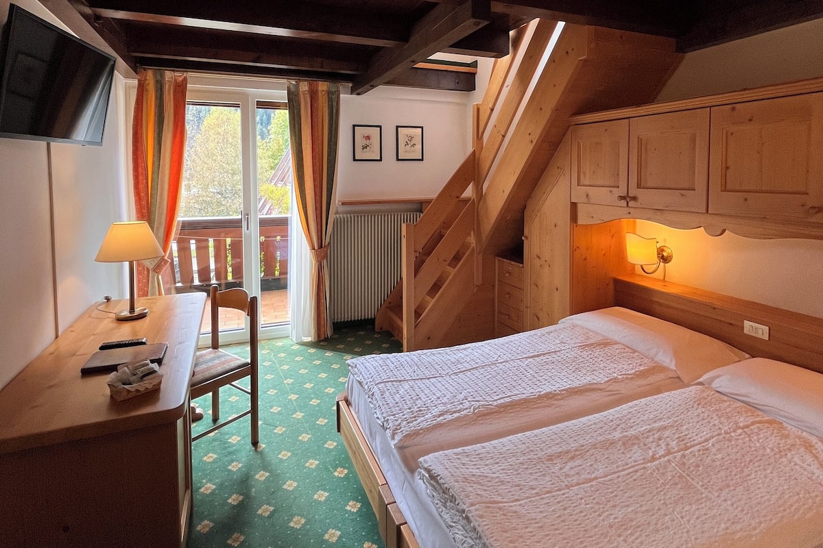 A bedroom with a bed, a desk, a chair, a window with curtains, and a staircase.