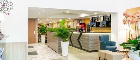 A modern hotel lobby with a reception desk, seating area, and a bar.