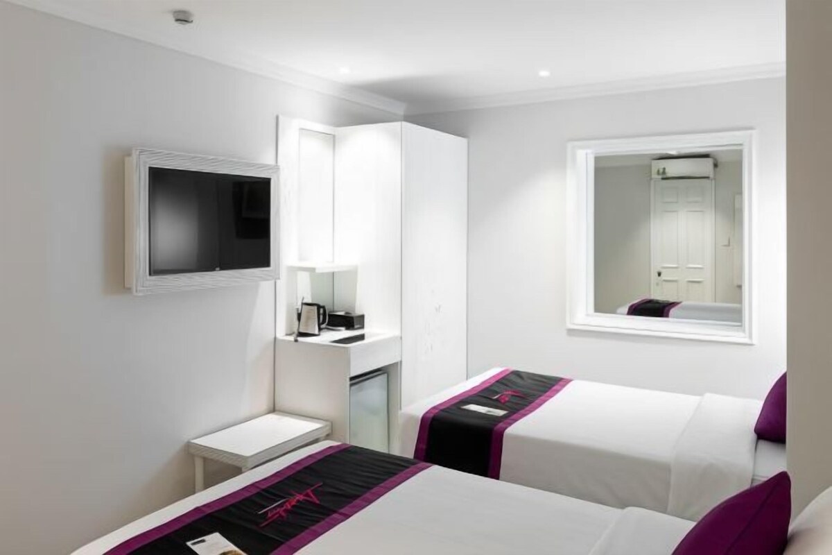 A hotel room with two beds, a TV, a desk, and a mirror.
