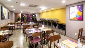 Un restaurant avec des tables et des chaises en bois, un mur d’accent jaune et un panneau néon indiquant qu’il est ouvert.