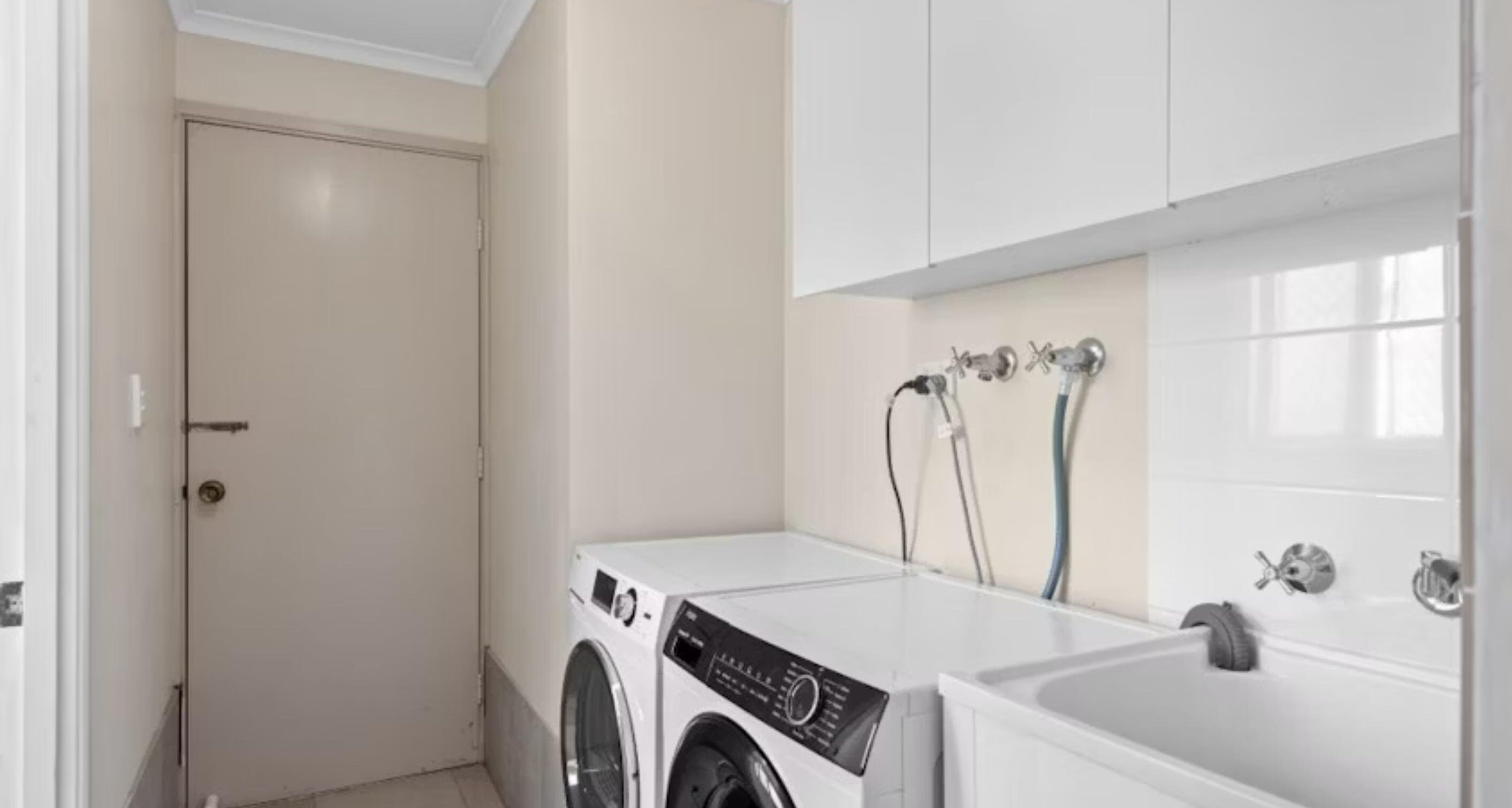 A laundry room with a washing machine and dryer, a sink, and a door.