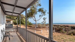 Un espacio al aire libre techado con una mesa y sillas, vista a la playa y un árbol.