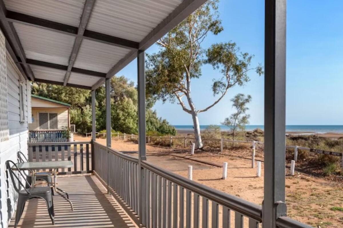 Ein überdachter Außenbereich mit Tisch und Stühlen und Blick auf den Strand, außerdem ein Baum.