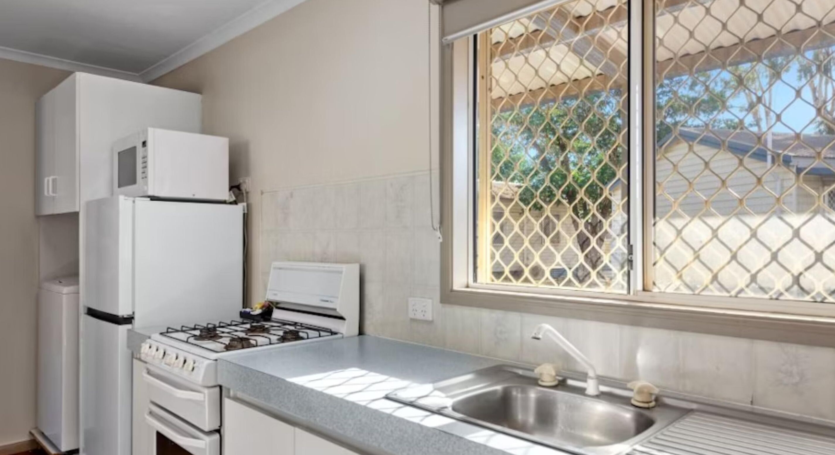 Una cocina con estufa a gas, un fregadero, un refrigerador y una ventana que ofrece vistas a árboles y edificios.