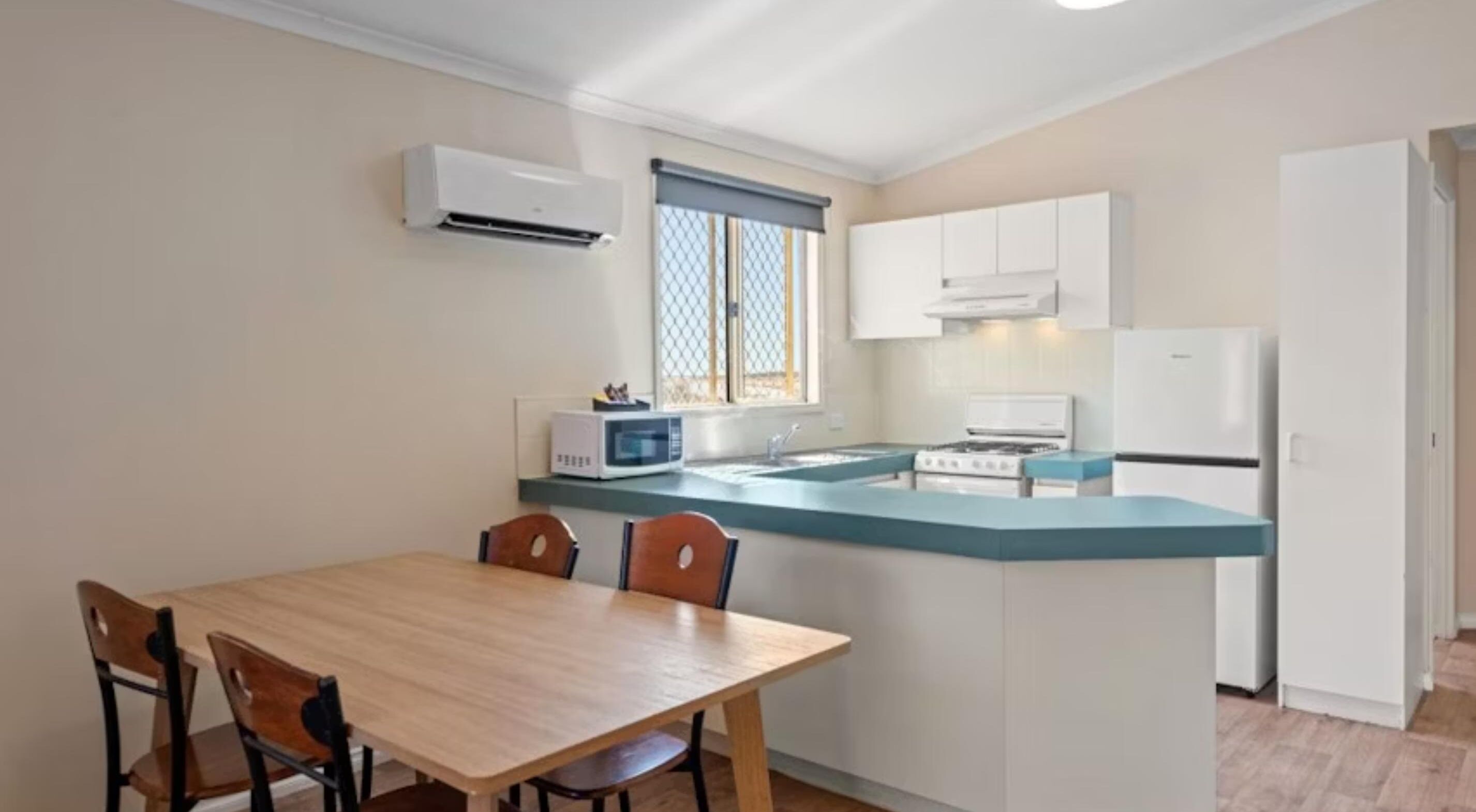 Une cuisine compacte dotée d’un îlot central, de meubles blancs, d’un four à micro-ondes, d’une cuisinière et d’un réfrigérateur.