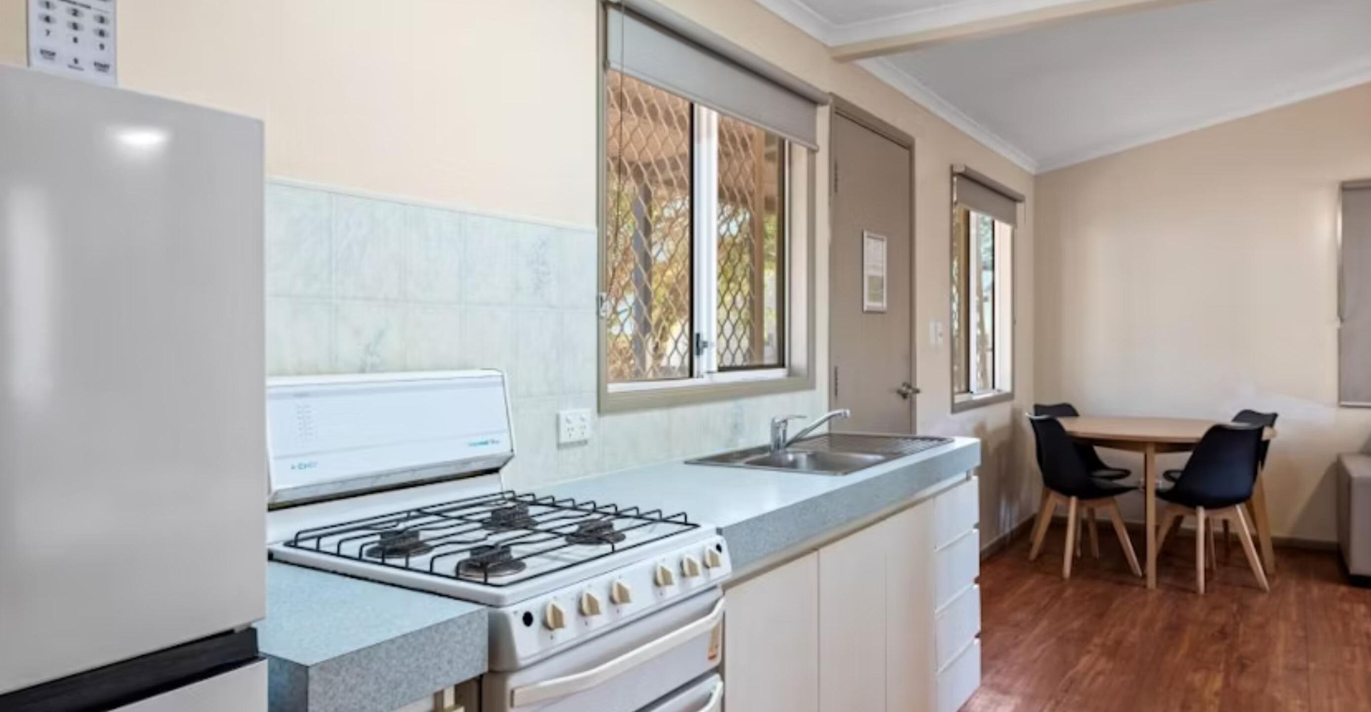 A compact kitchen with a gas stove, sink, and white cabinets. There is a dining area with a table and chairs.