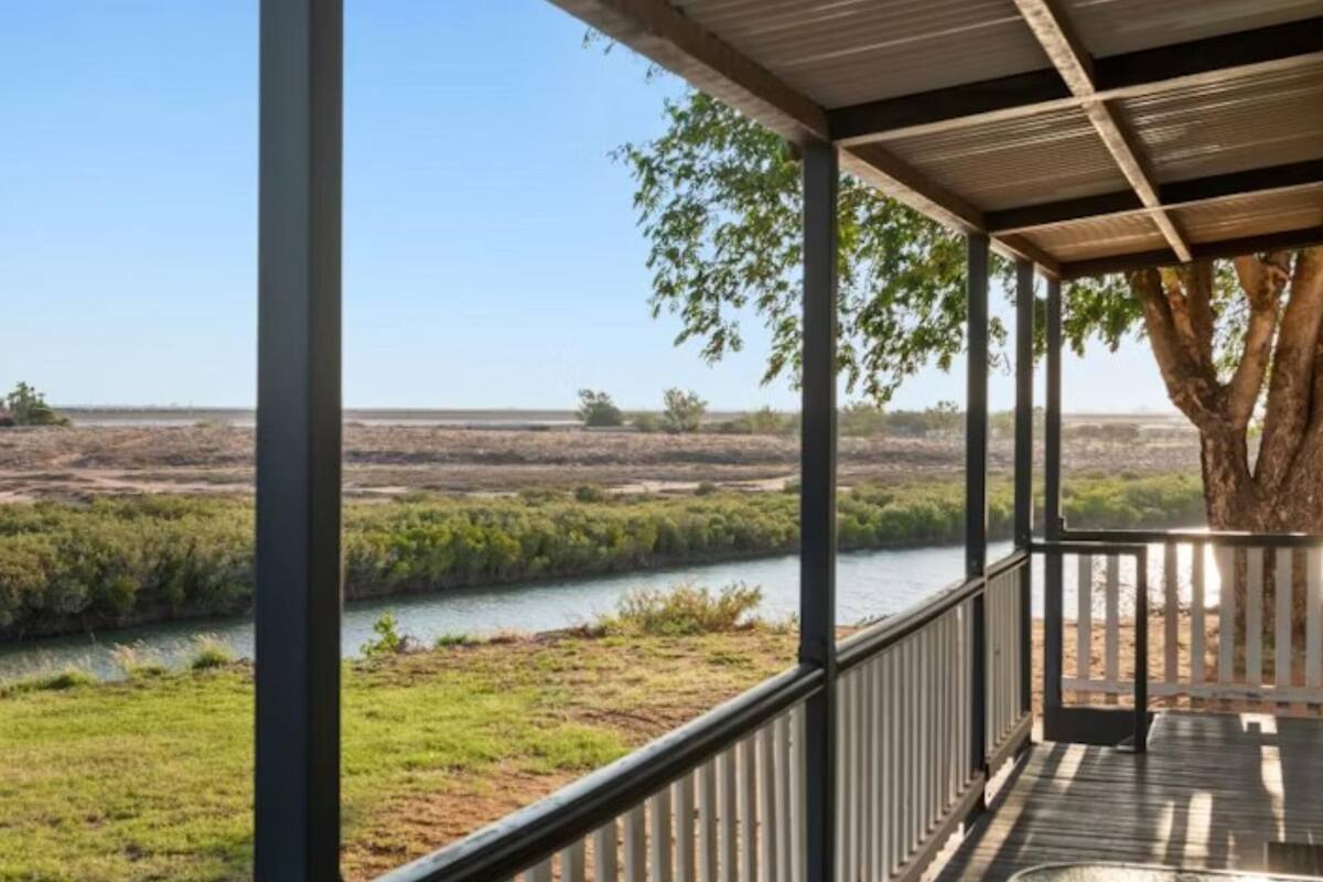 Eine überdachte Veranda mit Blick auf einen Fluss und offenes Gelände.