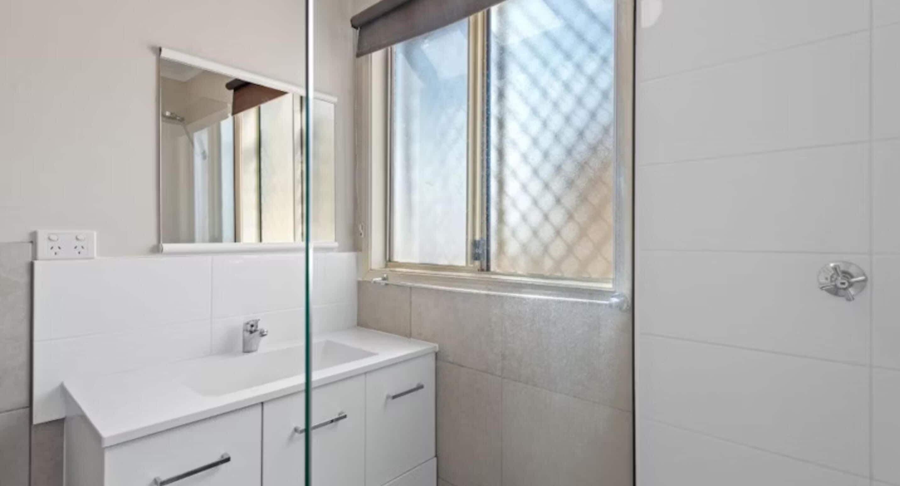 Une salle de bain moderne avec un meuble-lavabo blanc, un grand miroir et une fenêtre.