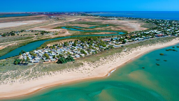 Vista aérea de una zona costera con playa, aguas cristalinas y un poblado con casas y vegetación.
