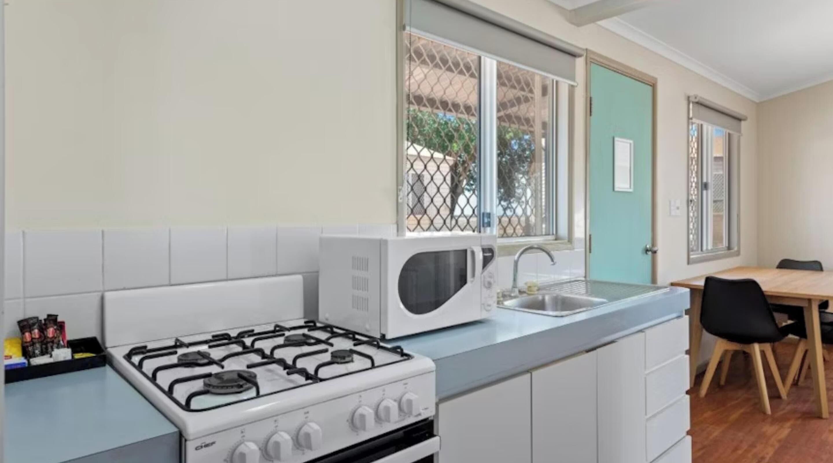 A compact kitchen with a gas stove, a microwave, a sink, and a dining area with a table and chairs.