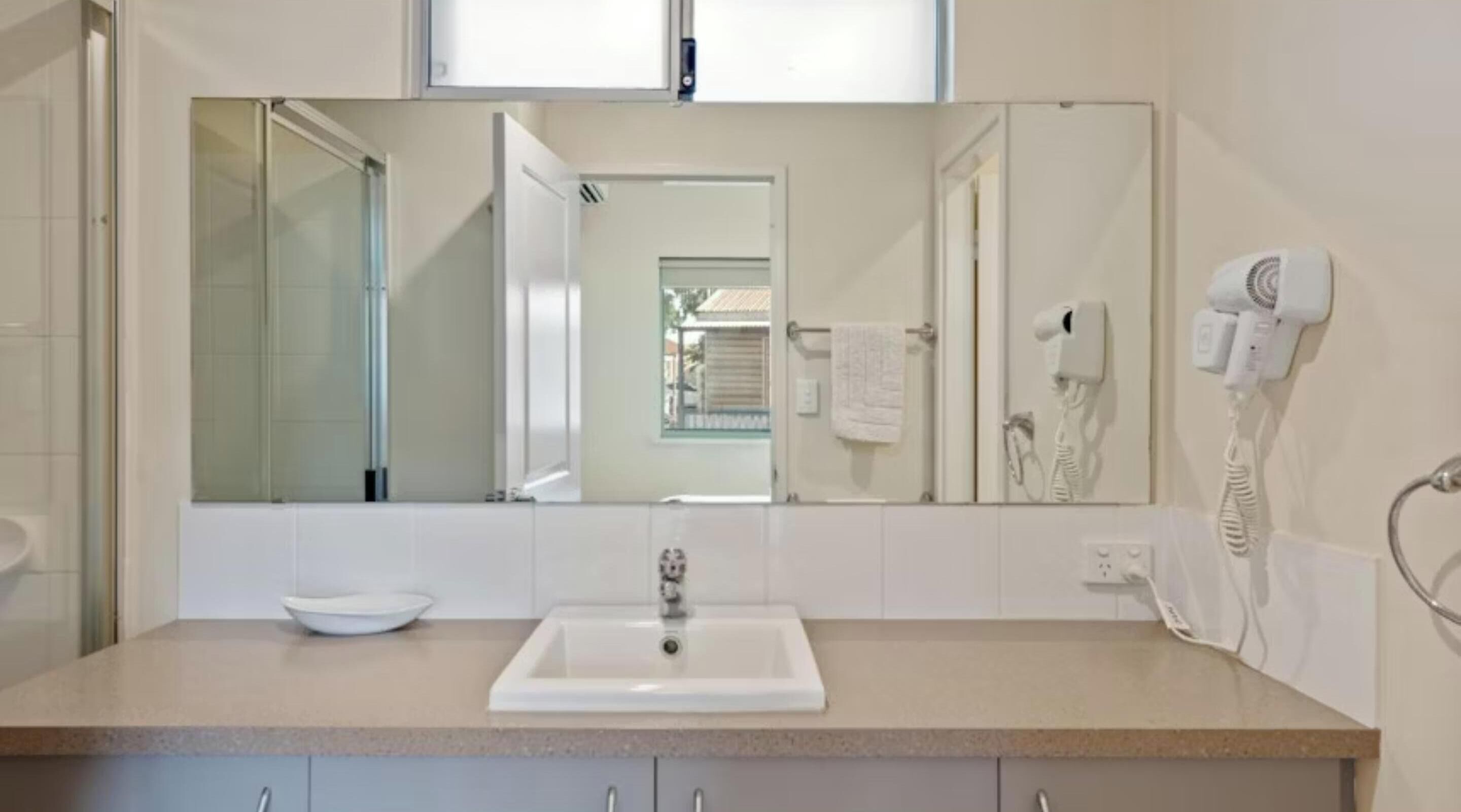 A bathroom with a large mirror, a sink, a hairdryer, and a towel rack.