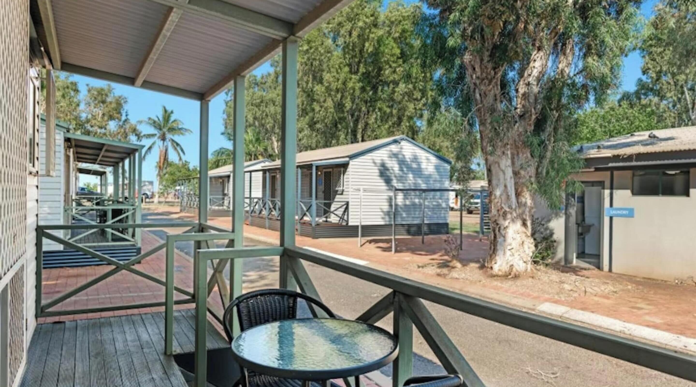 A covered outdoor area with a table and chairs, a building labeled "LAUNDRY", and a tree in the background.