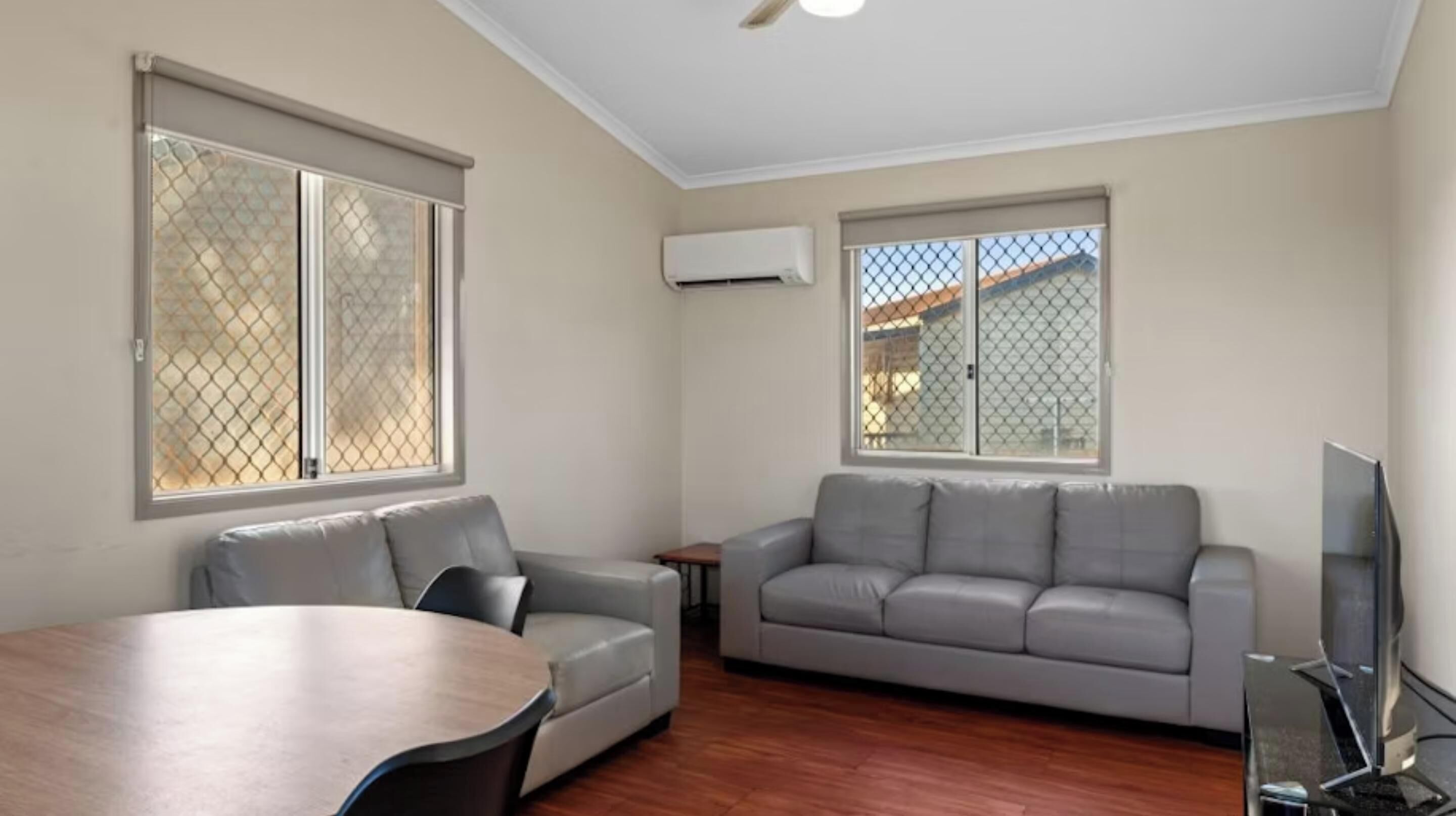 A living room with a grey sofa, a dining table, and a TV.