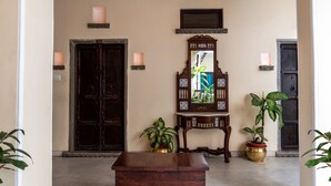 A hallway with a wooden chest, two potted plants, a mirror, and two doors. - Udaigarh (Udaipur)