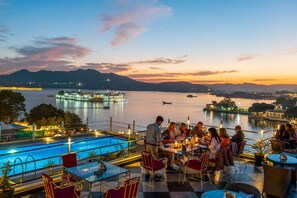 Un bar en la azotea con mesas y sillas, con vista a un lago y montañas al fondo.
