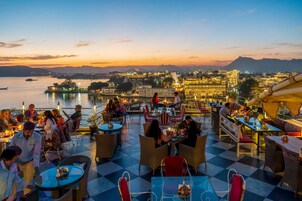 Una terraza con mesas y sillas, con vista a un cuerpo de agua y un paisaje urbano con edificios iluminados.