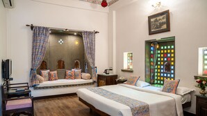 A bedroom with two beds, a wooden floor, a window with colorful lights, and a wall-mounted picture. - Udaigarh (Udaipur)