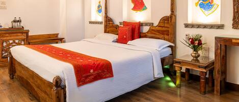 A traditional room with a large wooden bed, a small table with a vase, and artwork on the walls.