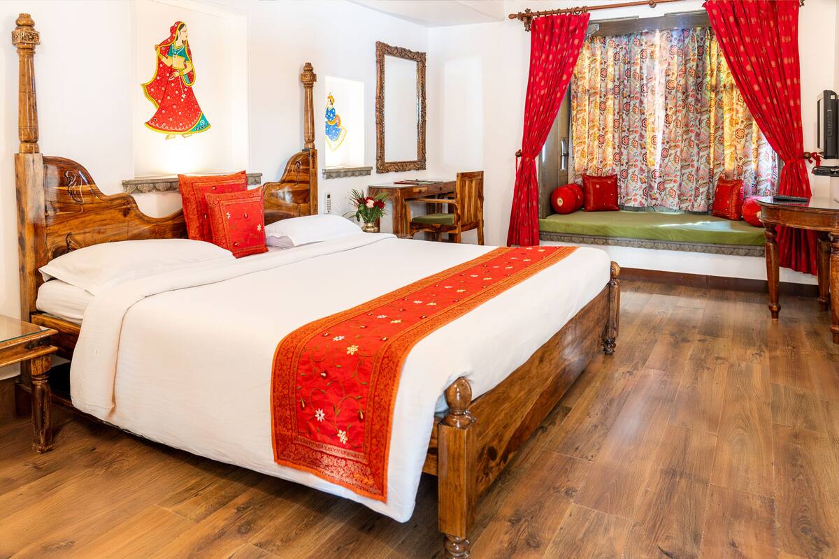 A traditional room with a large bed, wooden furniture, and a window with red curtains.